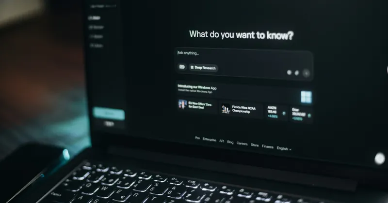 Laptop screen in a dark room showing an AI search box that asks "What do you want to know?"
