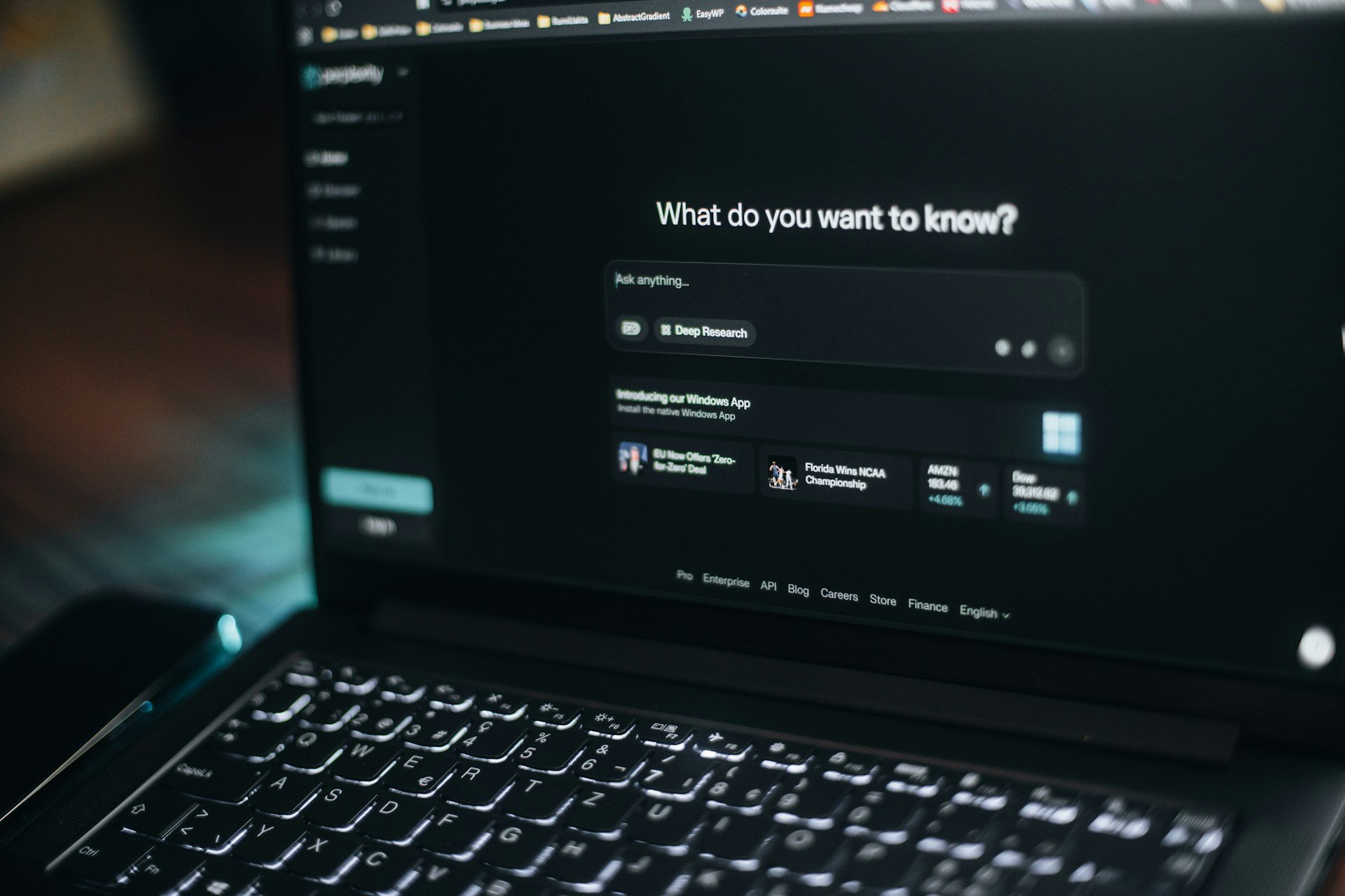 Laptop screen in a dark room showing an AI search box that asks "What do you want to know?"